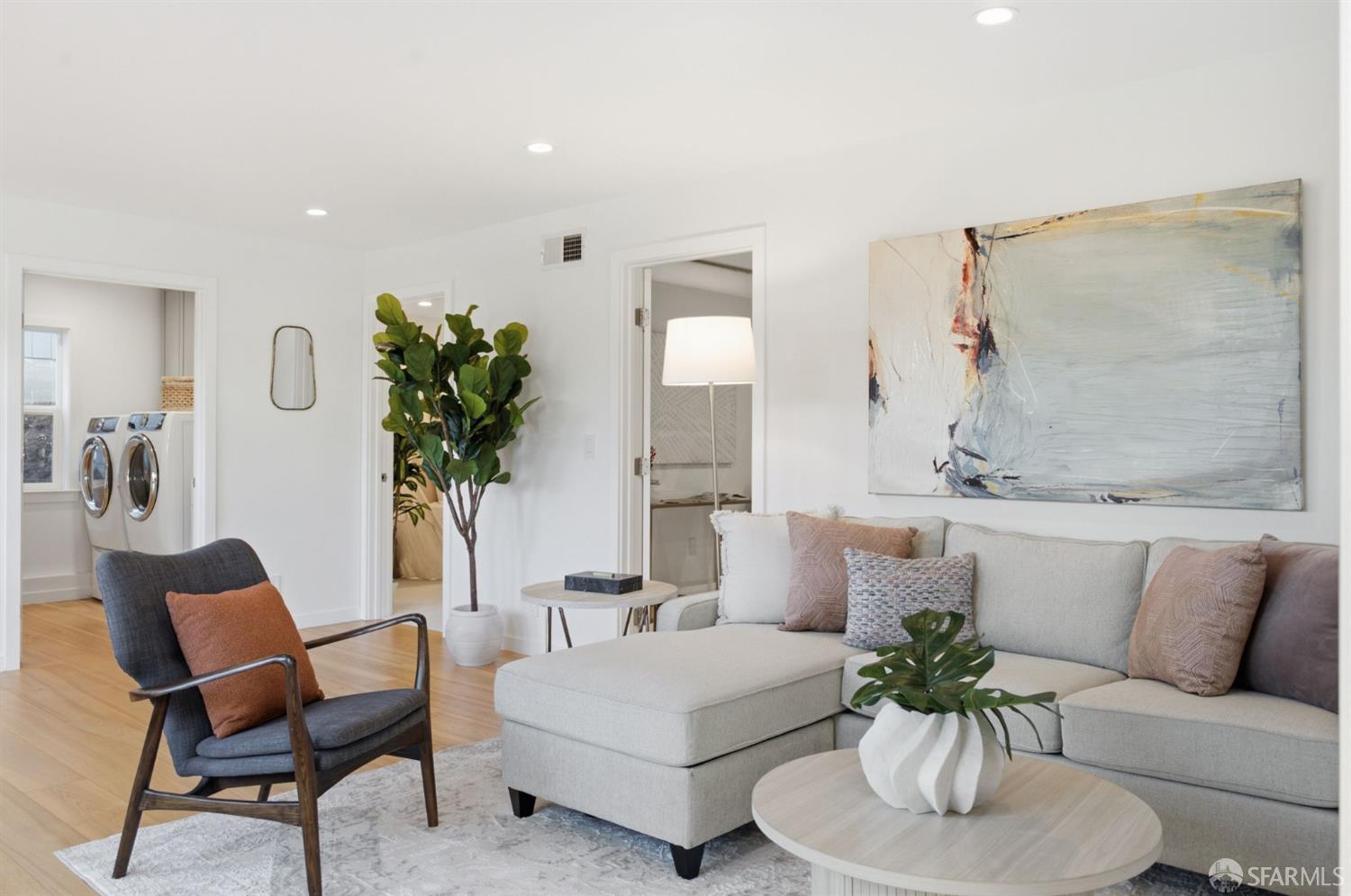 Living room with a light sectional sofa, dark armchair, and abstract wall art.