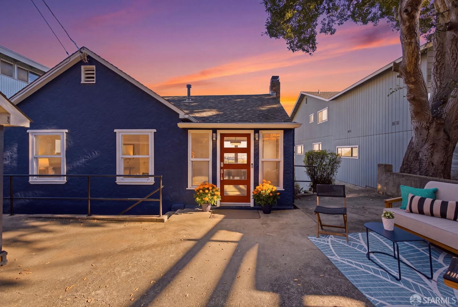 Blue cottage exterior and furnished patio beneath a colorful sunset.