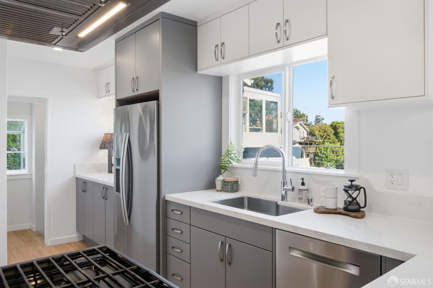 Modern kitchen with gray cabinets, stainless appliances, and a sink beneath a large window.