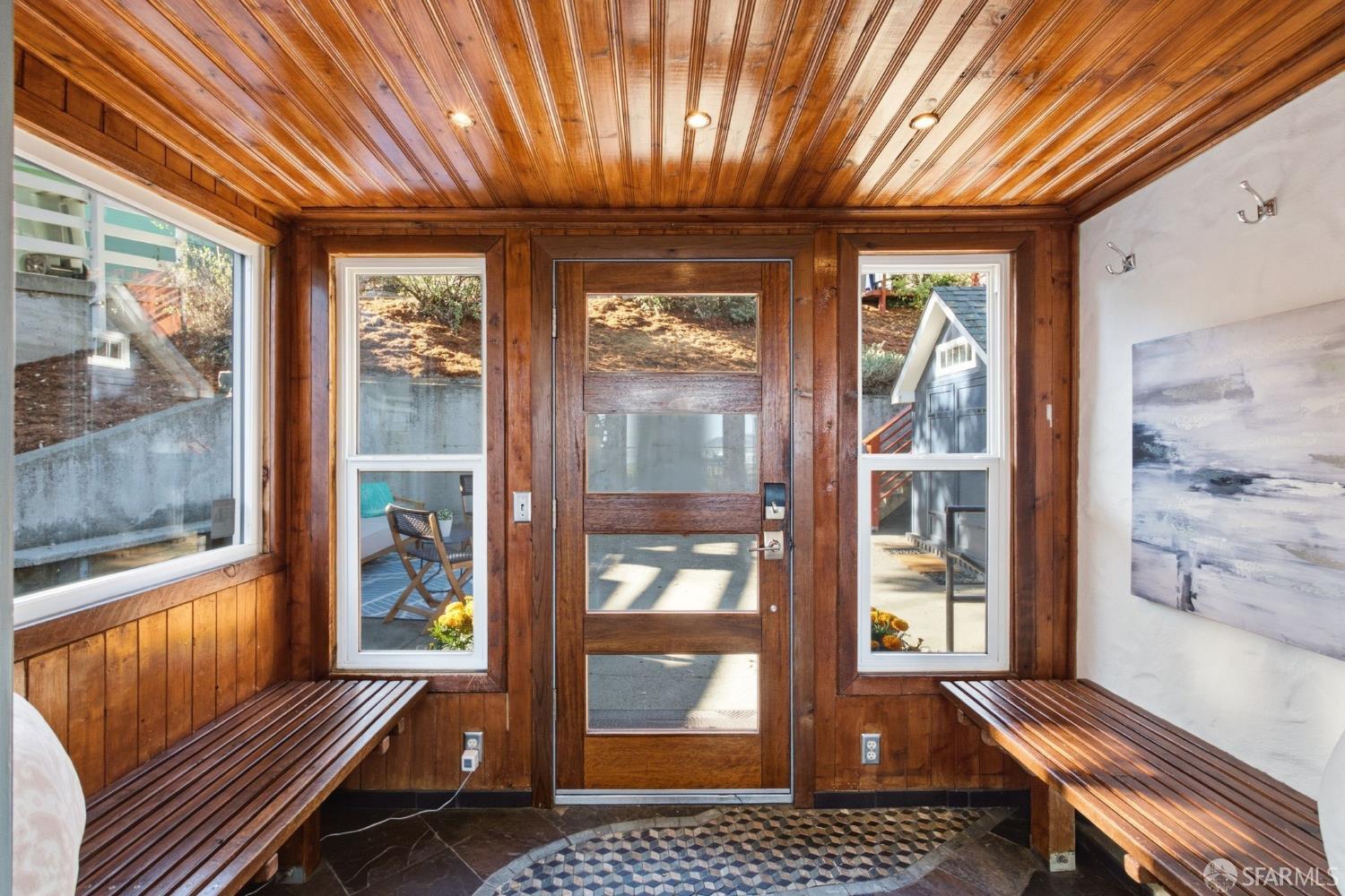 Wood-paneled entry vestibule with a glass door, built-in benches, and patterned tile floor.