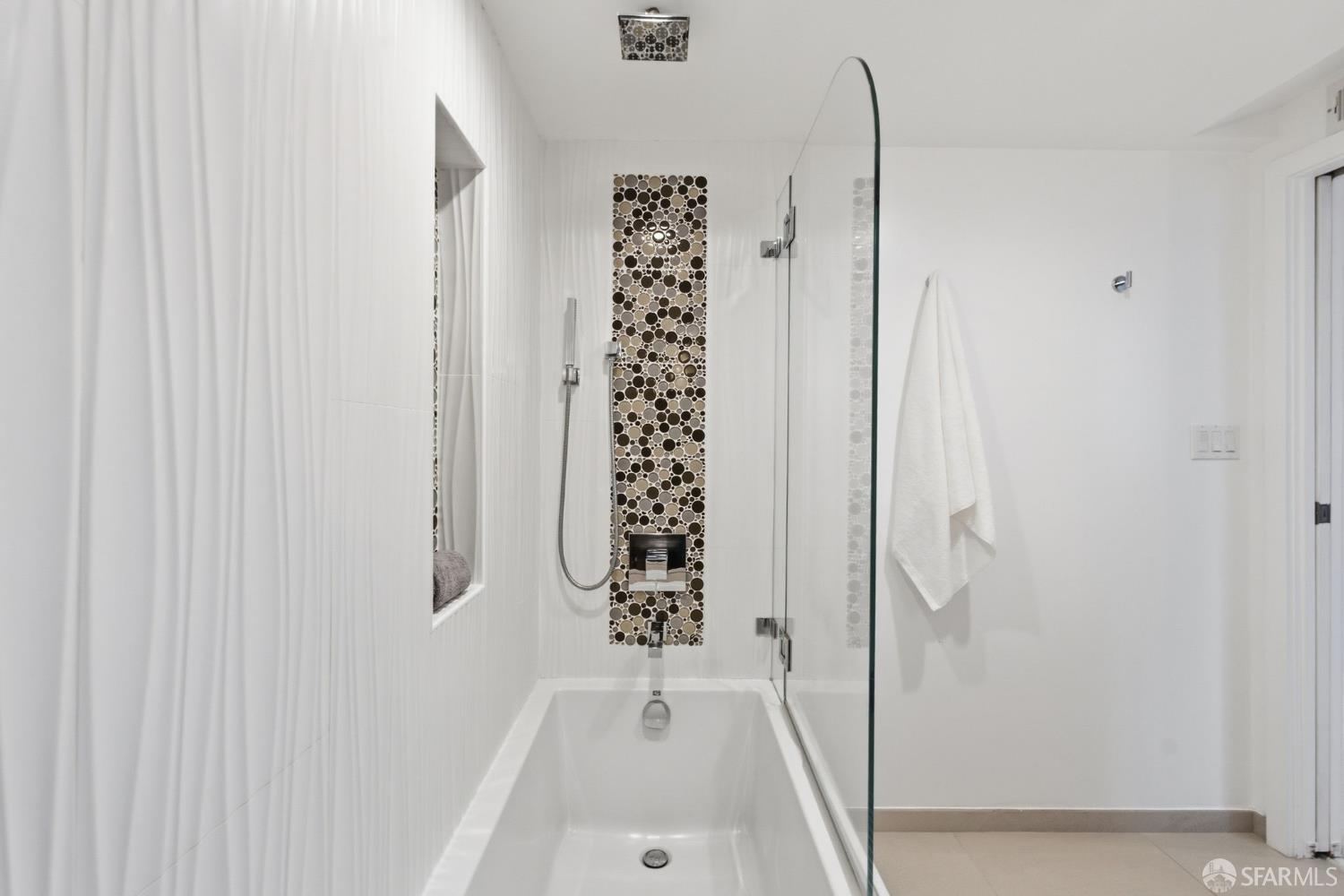 Bathroom with a bathtub, glass shower screen, and circular mosaic tile accent.