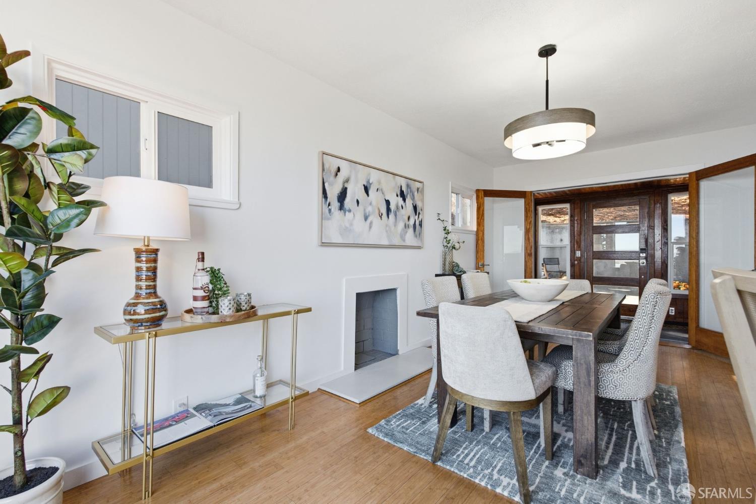 Dining room with a dark wood table, patterned rug, small fireplace, and wood-framed glass doors.