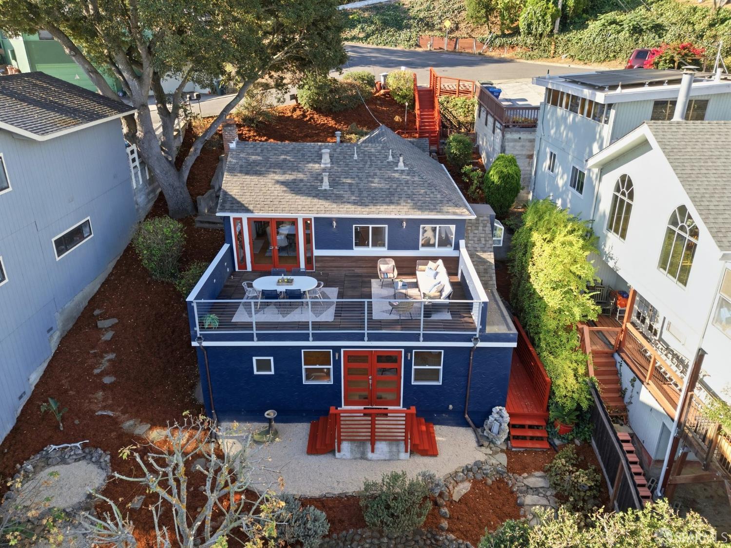 Aerial view of a blue home with a furnished deck and red stairs to the yard.