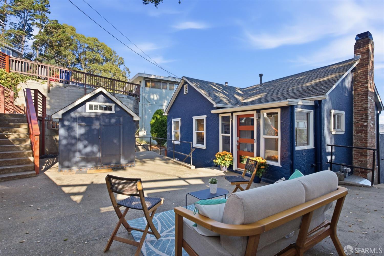 Blue home with a paved patio, outdoor seating, detached shed, and brick chimney.