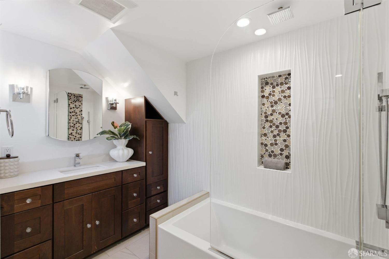 Bathroom with dark wood vanity, bathtub, and glass shower featuring a circular mosaic-tile niche.