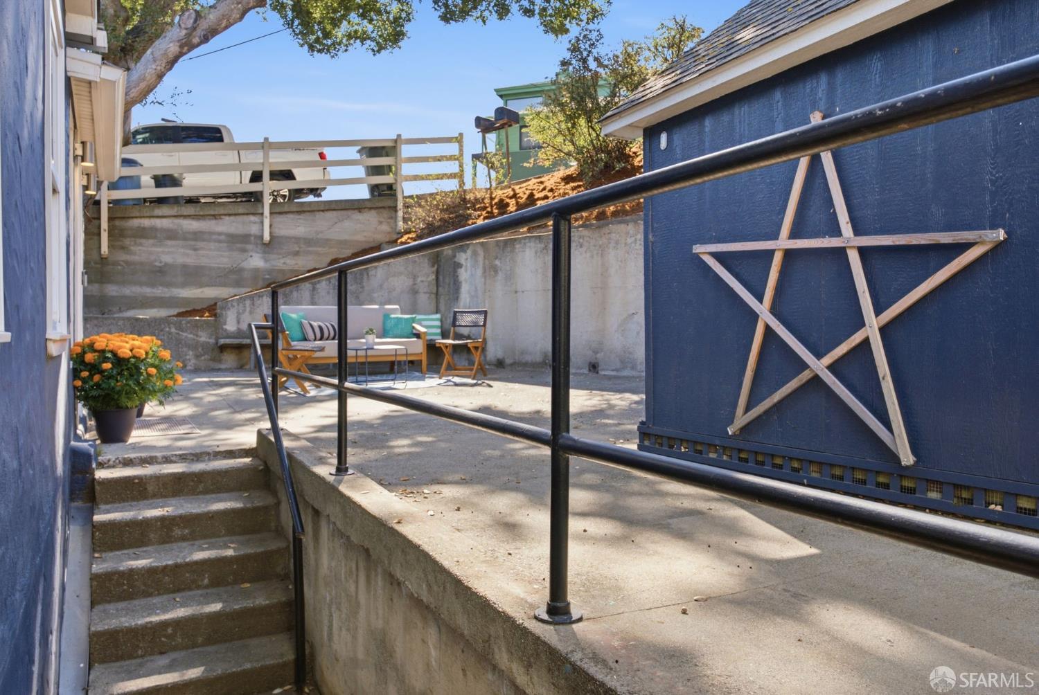 Outdoor patio with concrete steps, black railings, seating, and a wooden star on a blue wall.