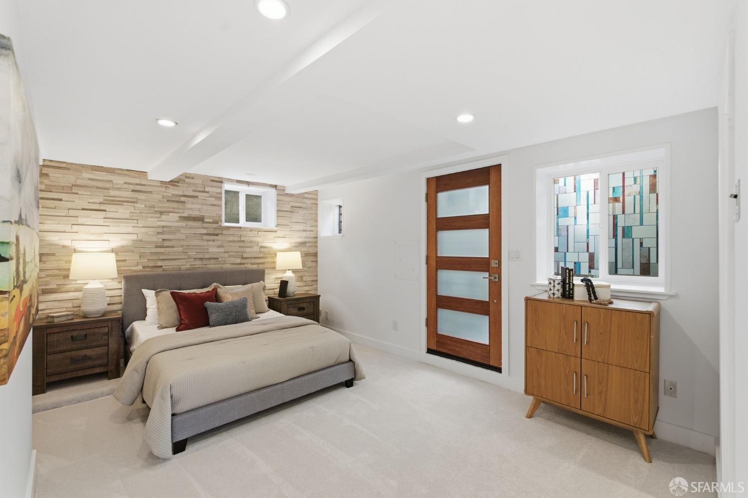 Staged bedroom with a stone accent wall, modern wood door, and colorful stained-glass window.