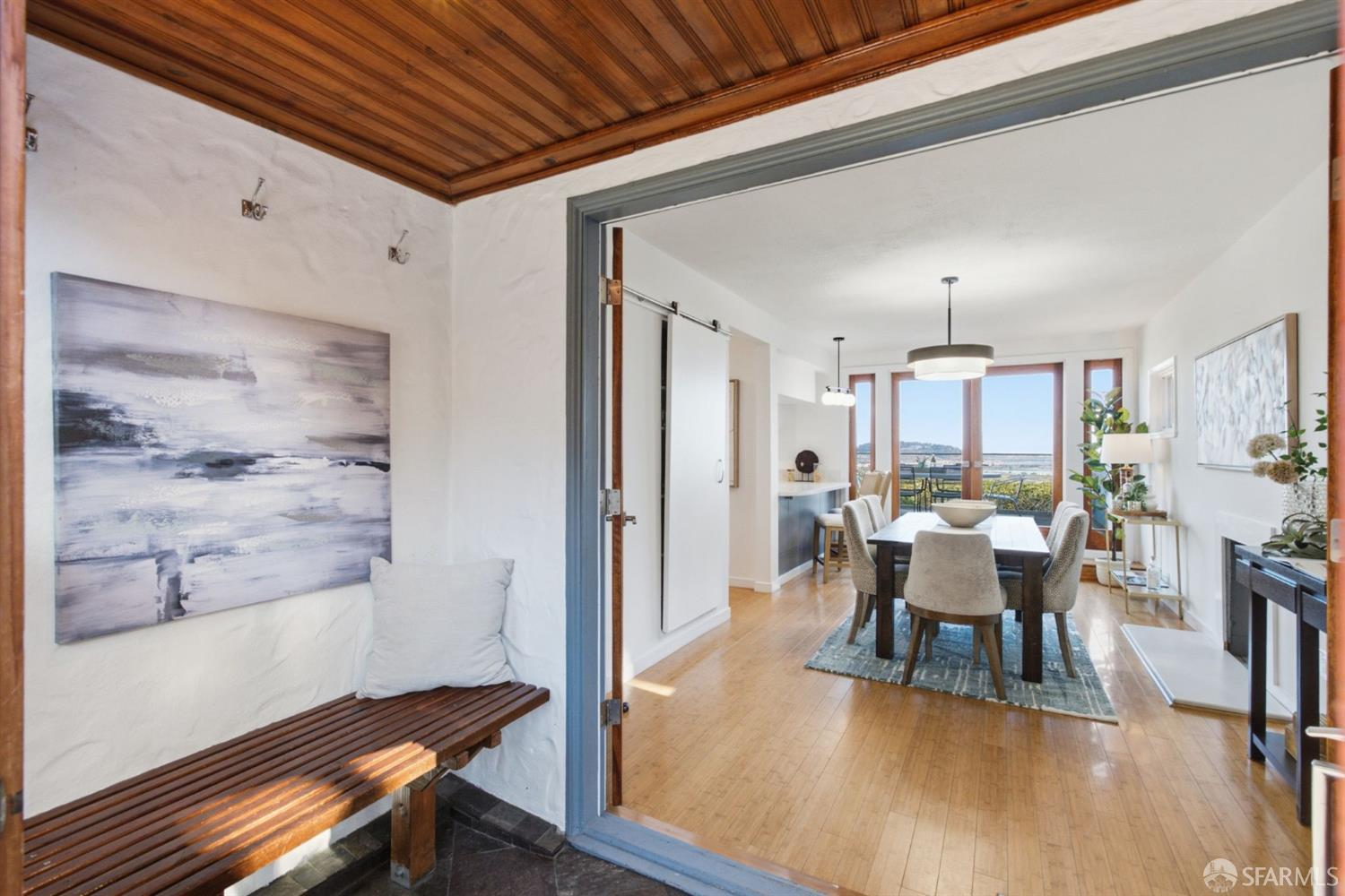 Entryway with a wood-paneled ceiling opens into a dining room with a water view.