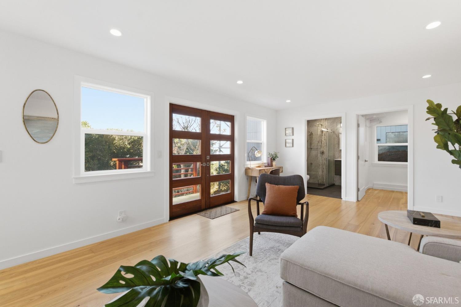 Bright living room with wood floors, a gray sofa, and dark wood-and-glass entry doors.