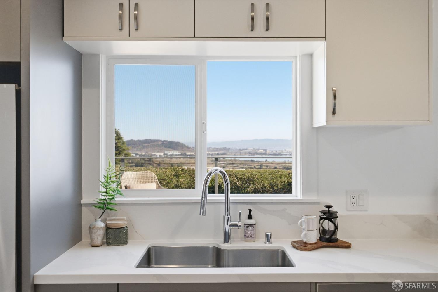 Kitchen sink beneath a large window overlooking greenery, hills, and distant water.
