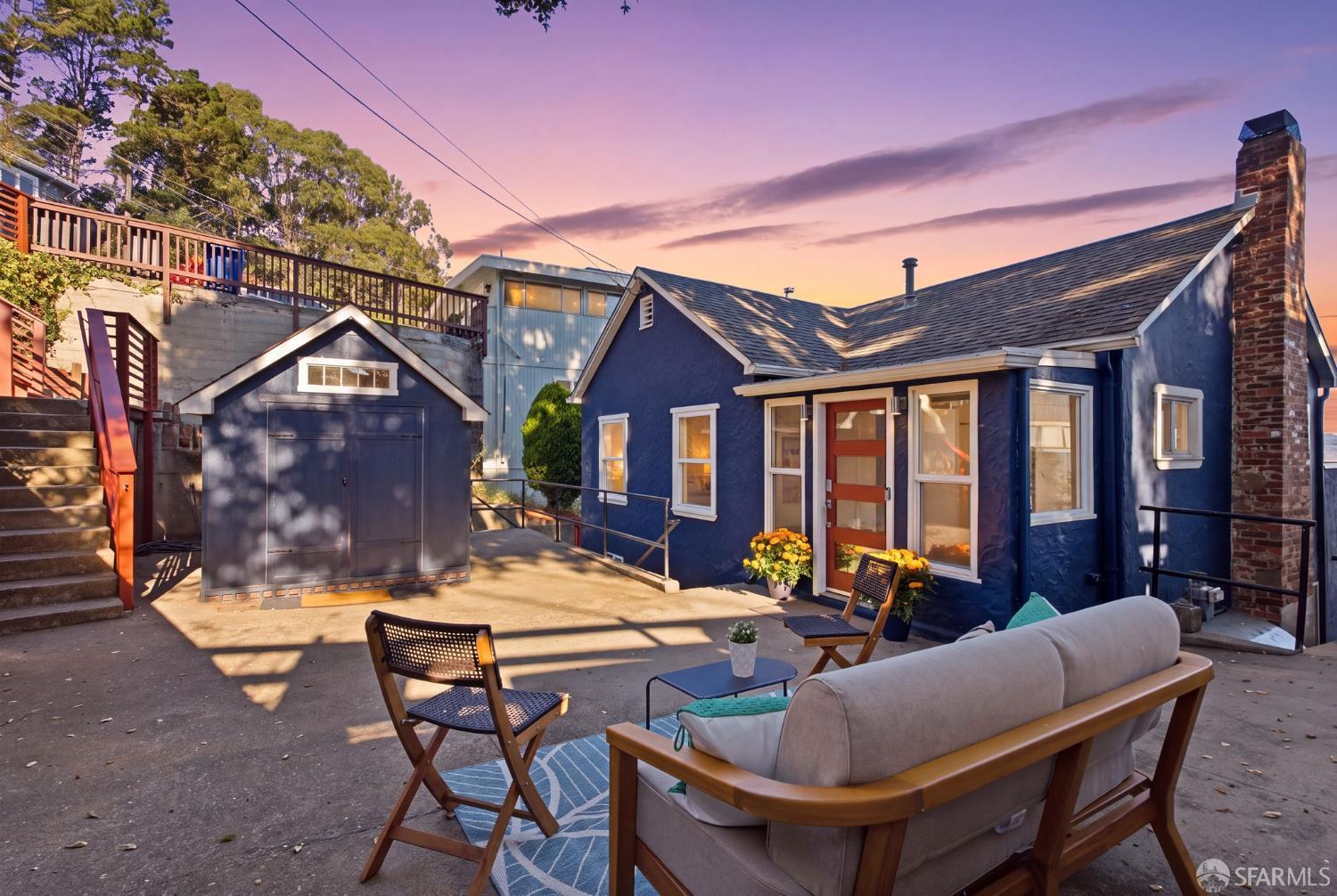 Blue house and detached garage beside a furnished patio at dusk.