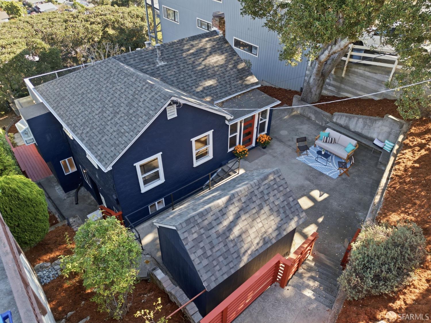 Aerial view of a dark blue house and paved courtyard with a furnished patio and detached outbuilding.
