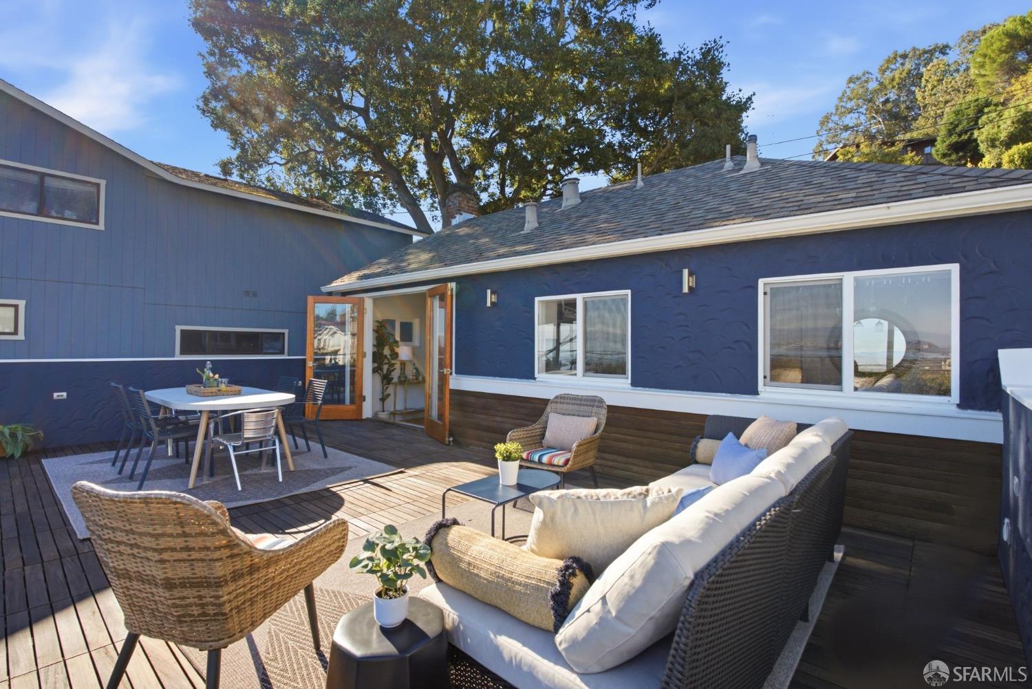Furnished patio with wood decking, outdoor dining set, and wicker lounge seating beside a blue home.