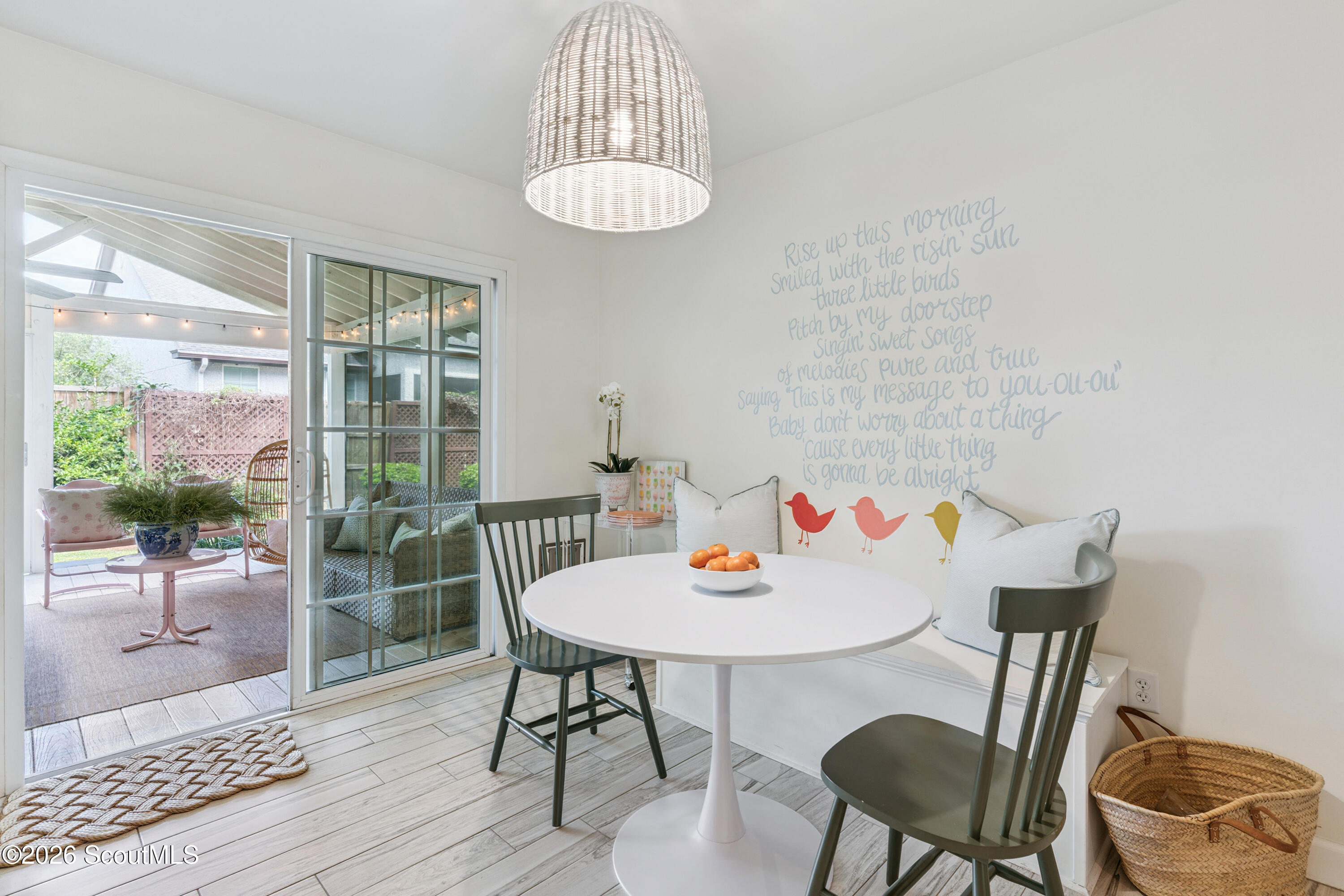 Dining nook with a white round table, built-in bench, bird mural, and sliding doors to a covered patio.