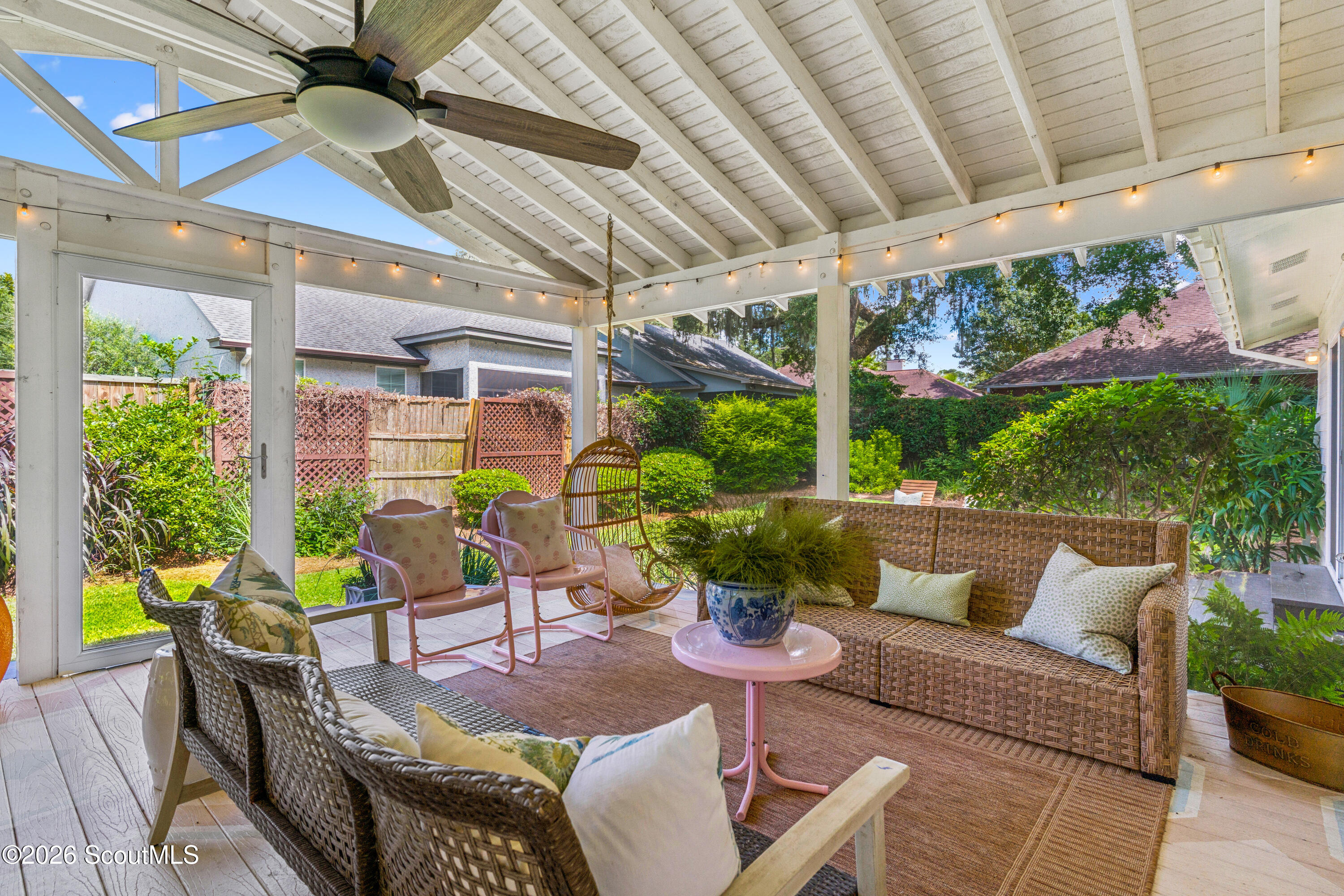 Covered patio with wicker seating, a ceiling fan, and views of a lush garden.