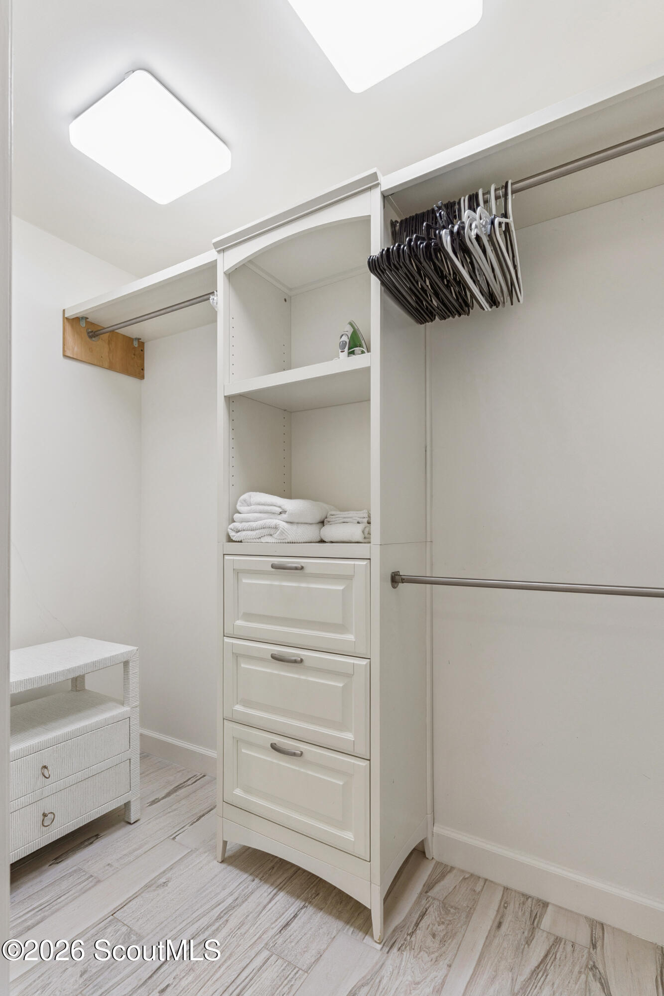 Walk-in closet with white built-in drawers, shelves, hanging rods, and folded towels.