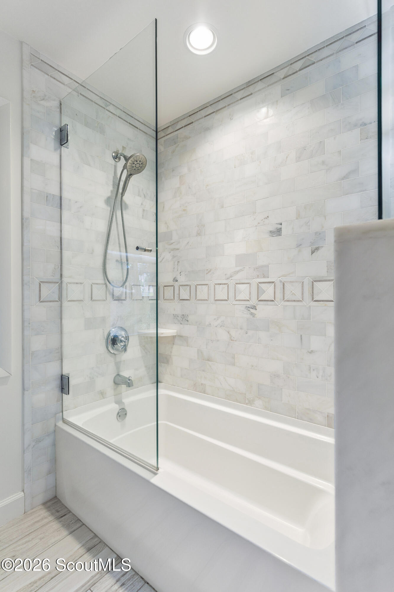 Bathroom tub and shower with a glass screen and marble-look tile.