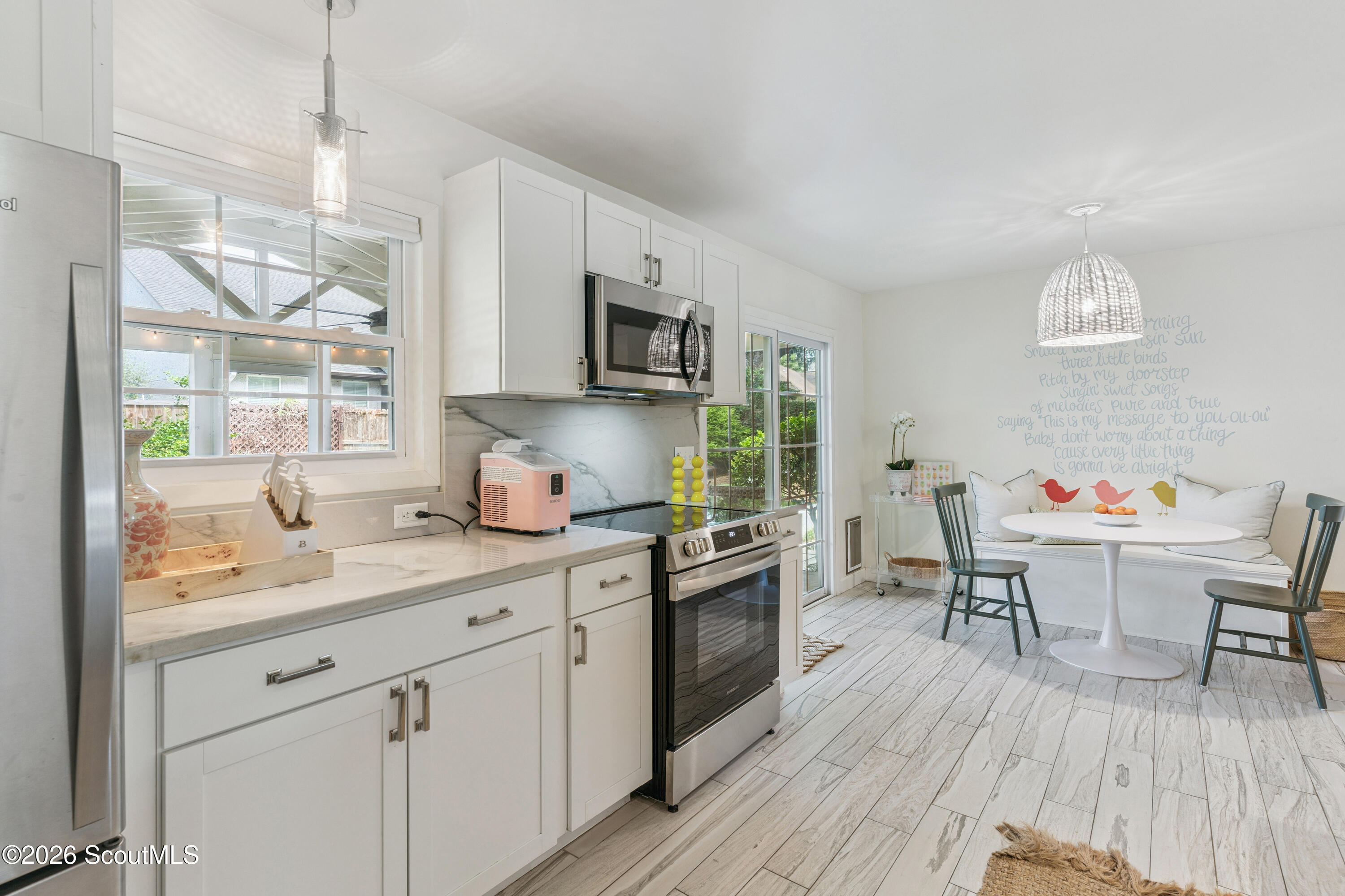 Bright white kitchen with stainless appliances and a dining nook with a banquette and round table.
