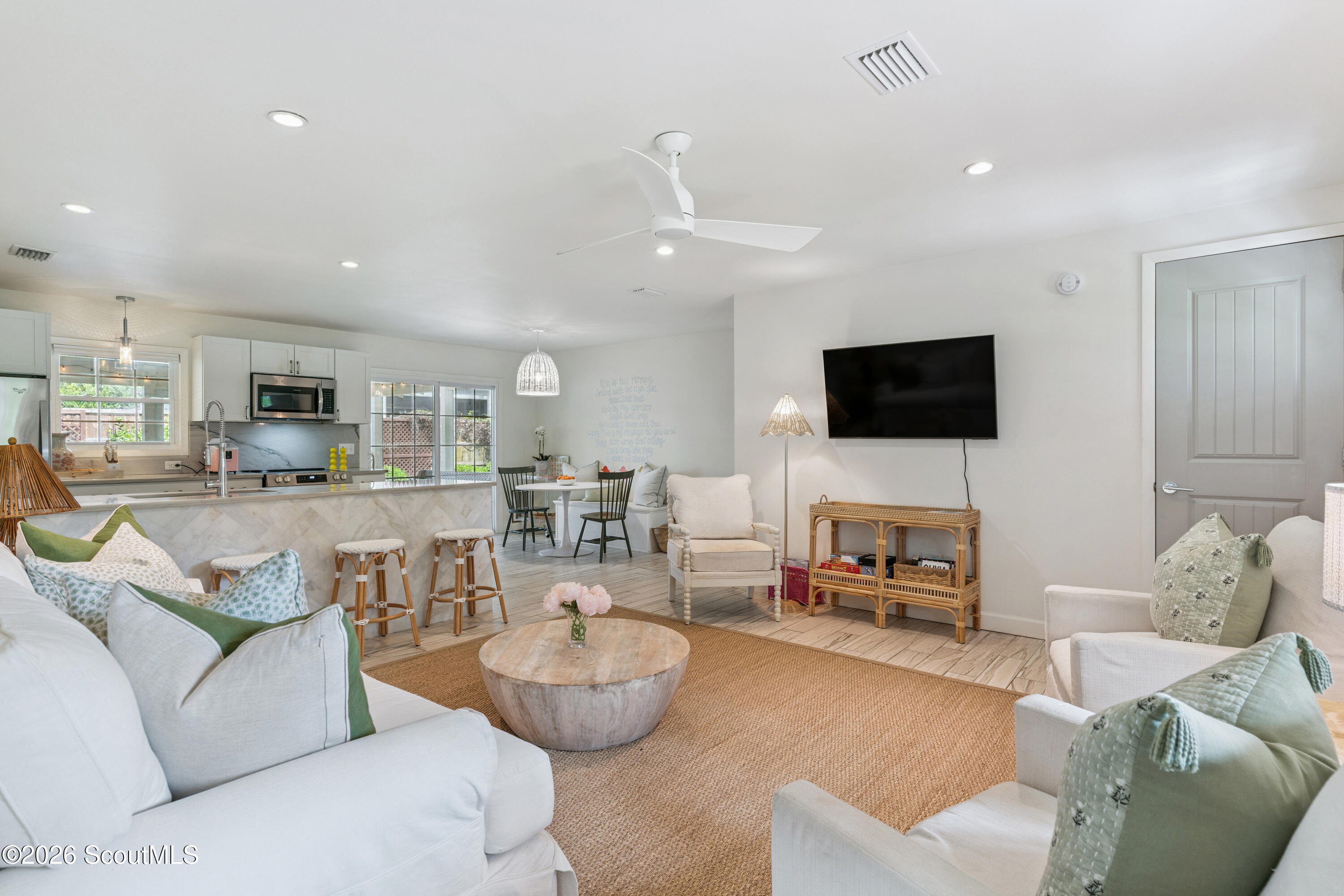 Open-plan living room with white sofas, a woven rug, and an adjoining kitchen with a breakfast bar.