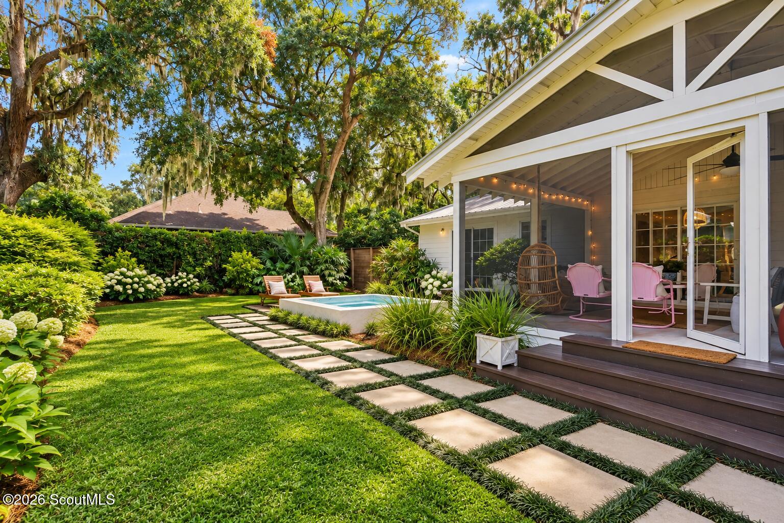 White home's covered rear deck beside a small pool, landscaped lawn, and stepping-stone path.