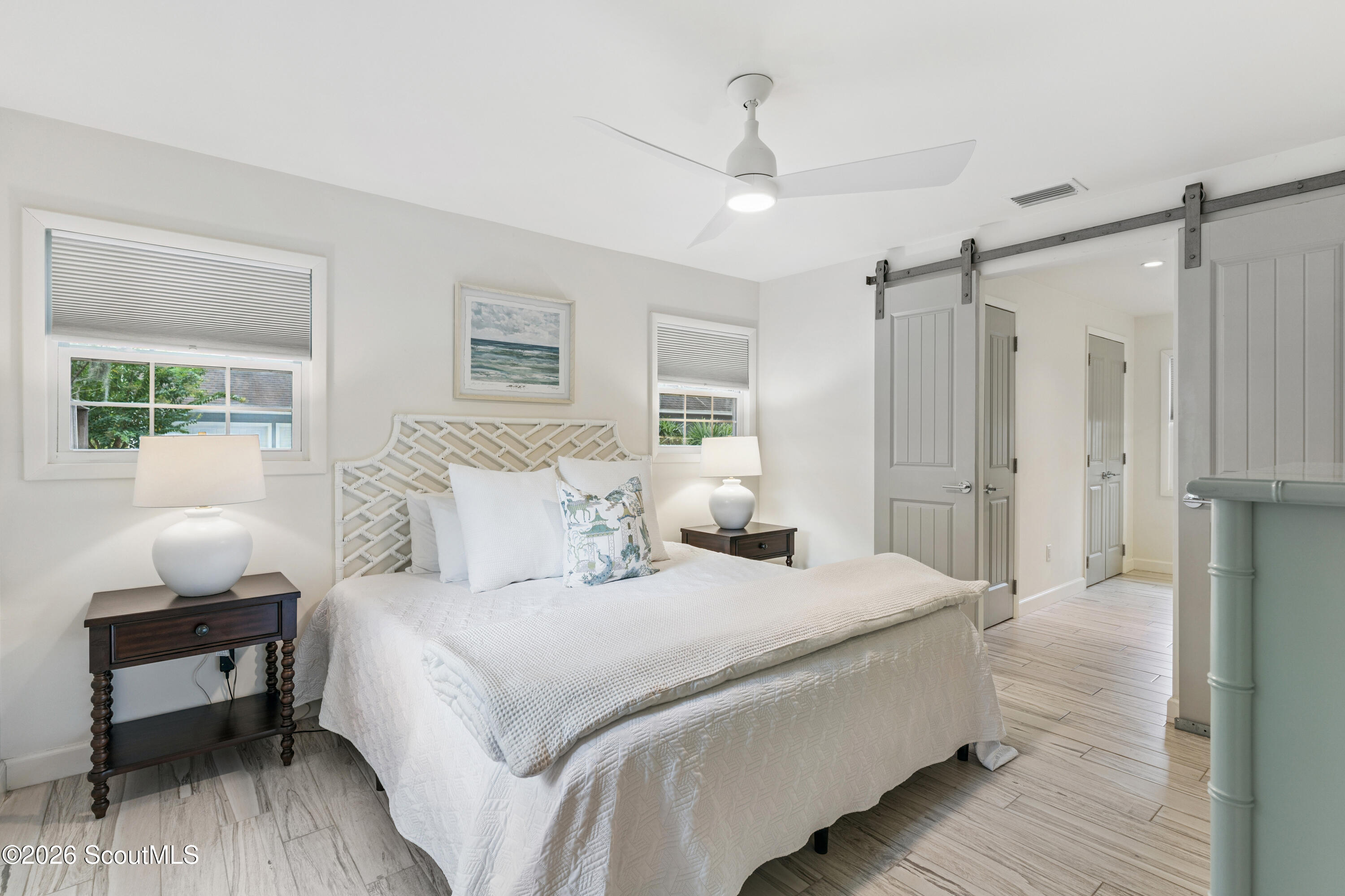 Bright bedroom with a white bed, woven headboard, two windows, and a gray sliding barn door.