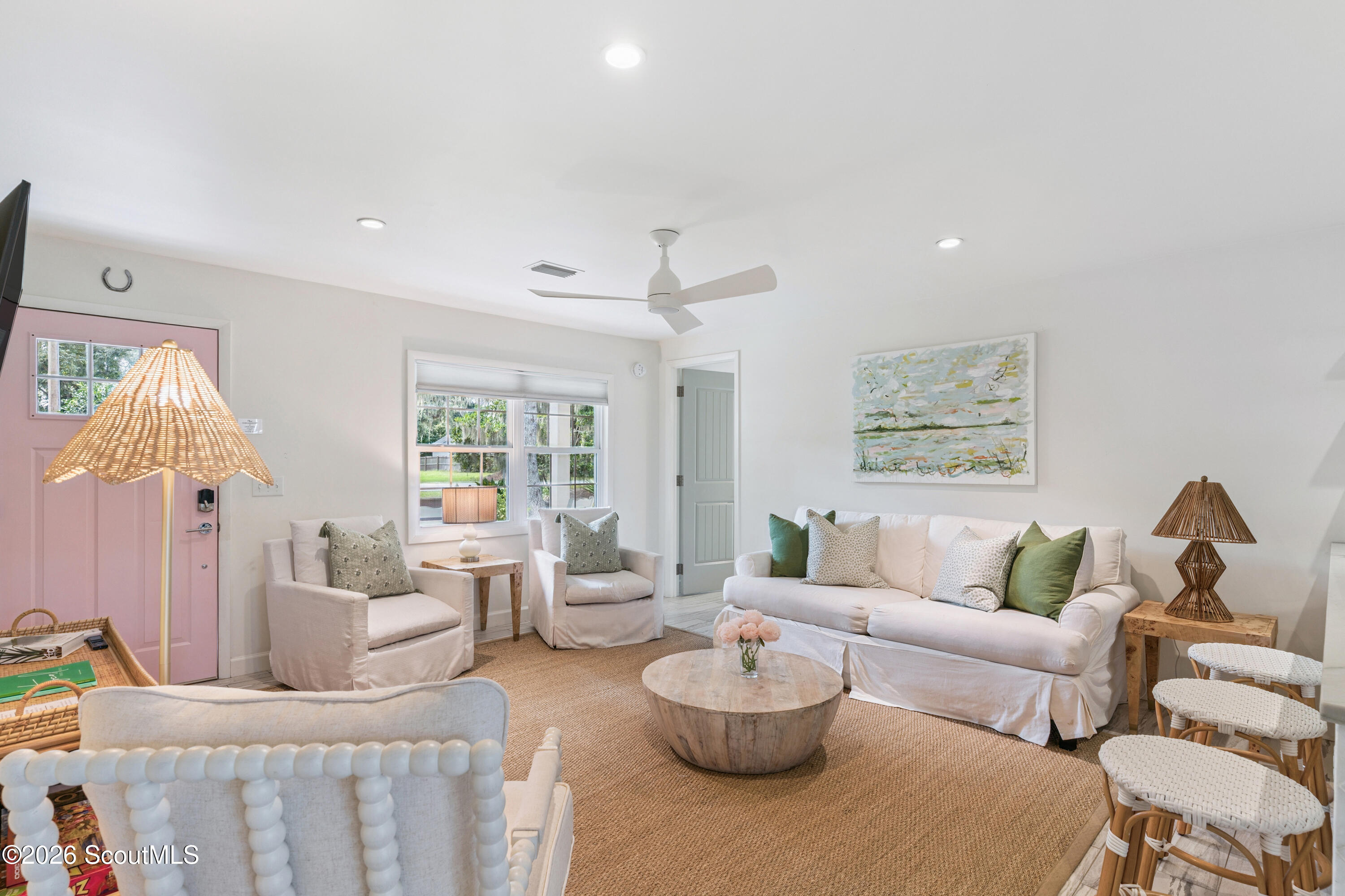 Bright living room with white slipcovered seating, a pink front door, and green accent pillows.