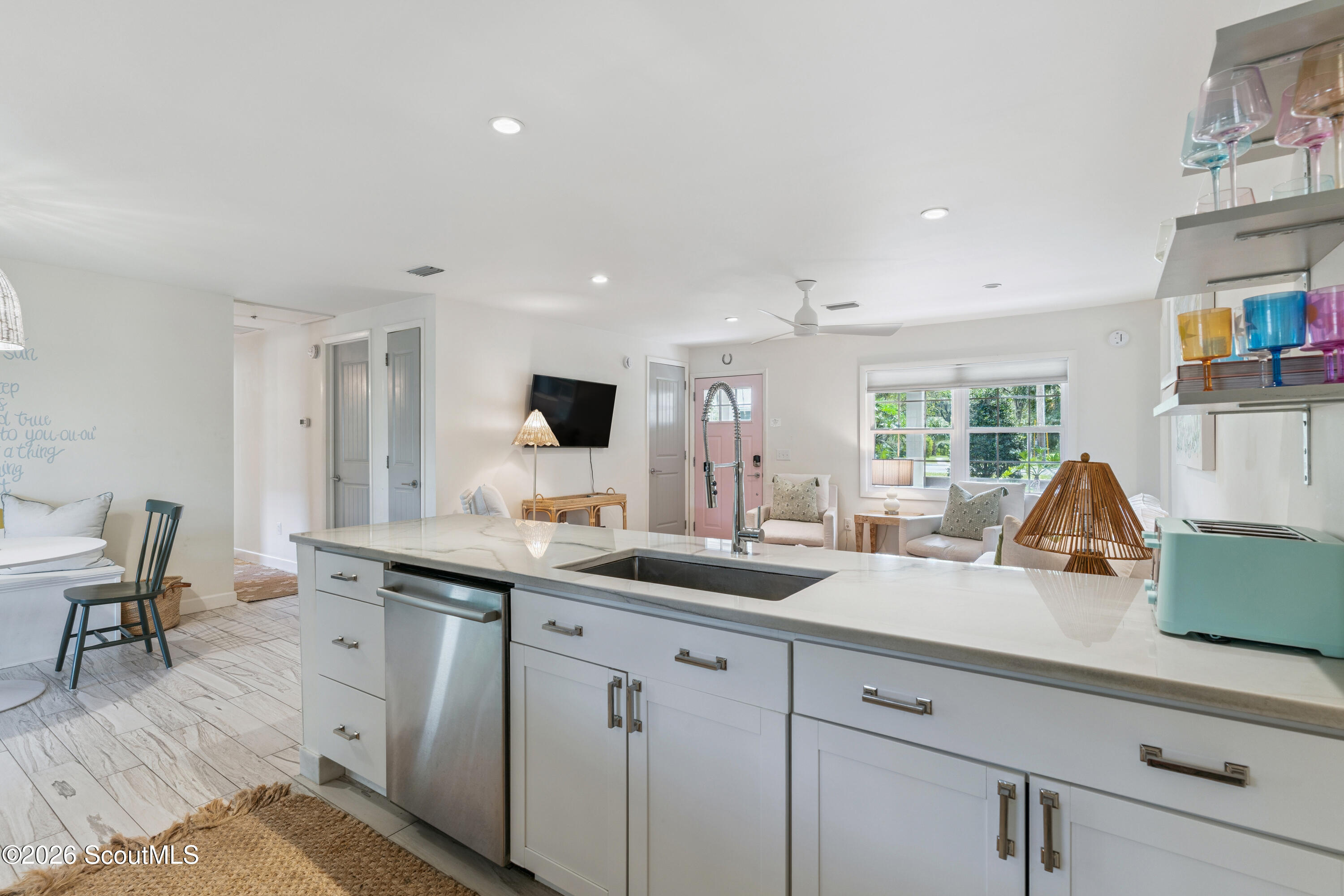 Open kitchen with a long white island and sink overlooking a furnished sitting area and large windows.