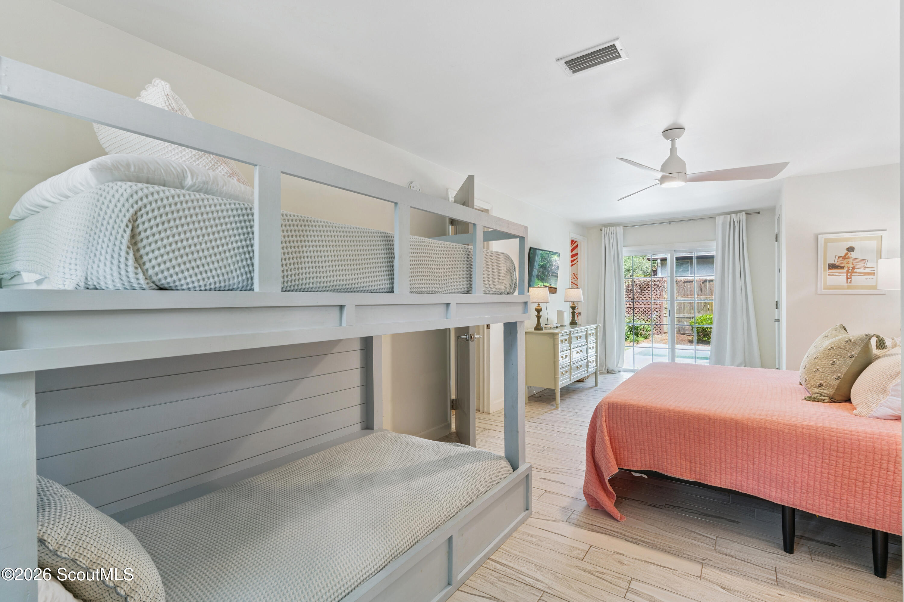 Bedroom with a gray built-in bunk bed and coral-covered bed beside sliding glass doors.