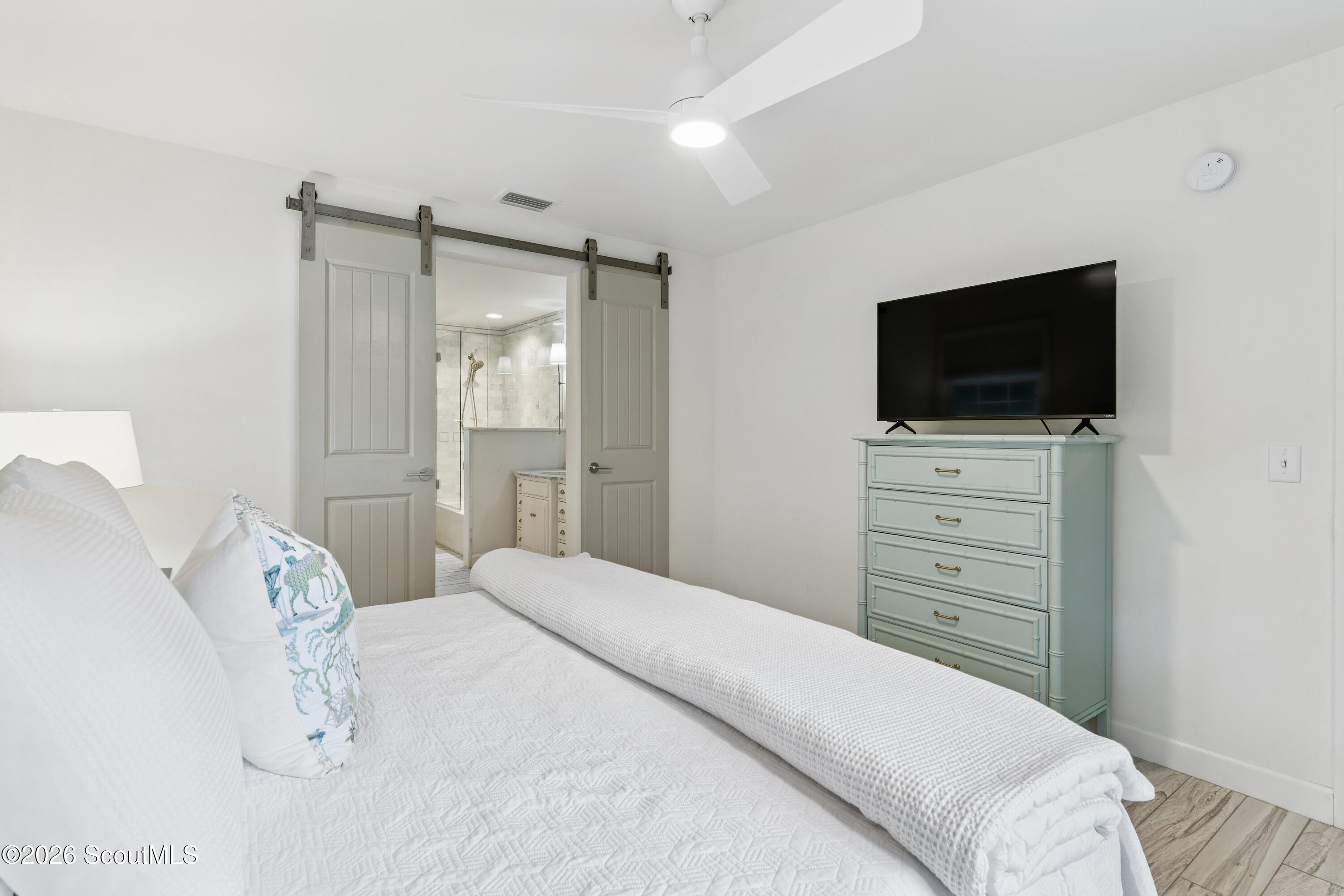 Bedroom with a white quilted bed, pale blue-green dresser, and sliding barn doors to an en suite bathroom.