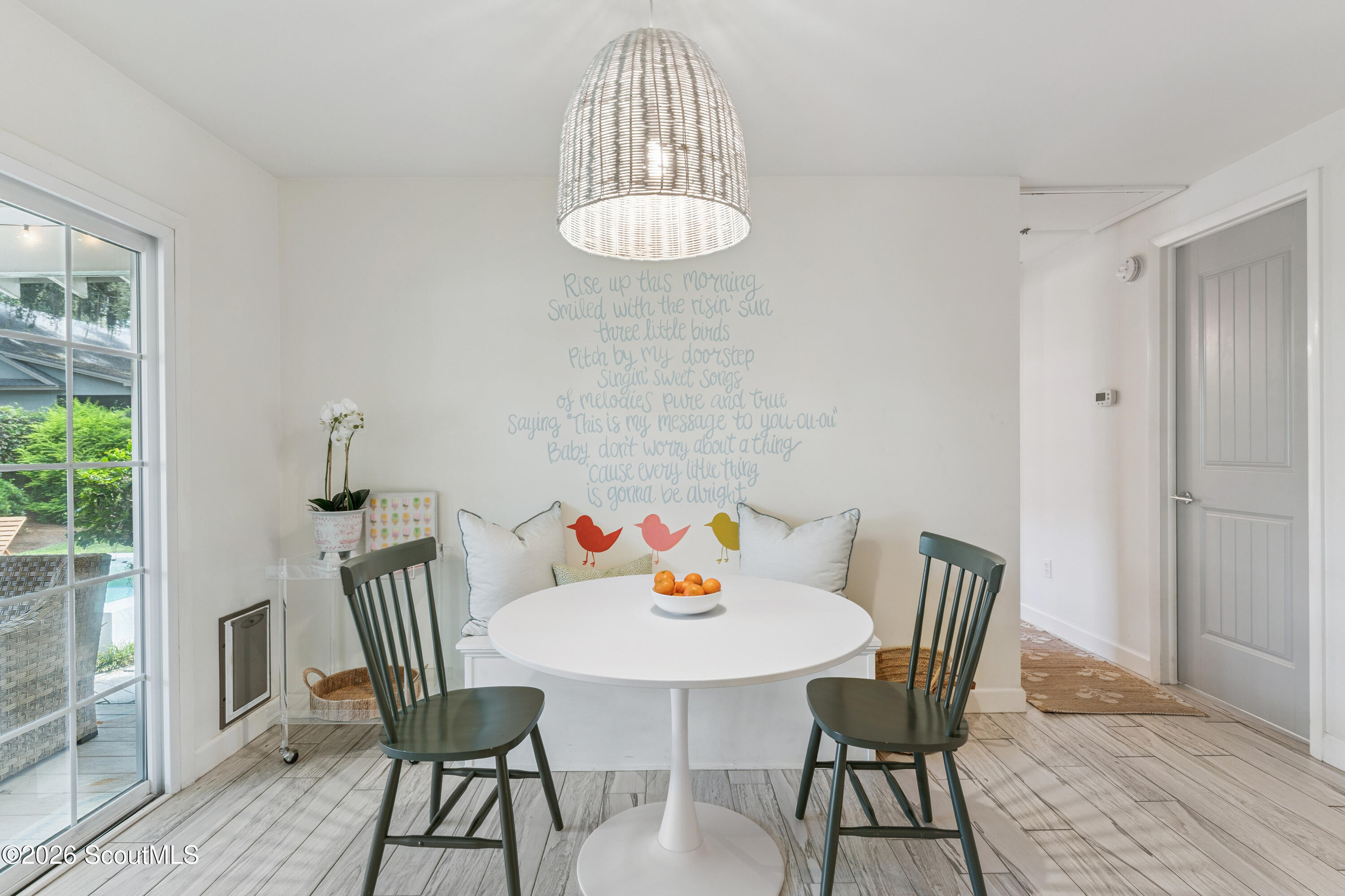 Dining nook with round white table, green chairs, bird-accented bench, and handwritten wall lyrics.