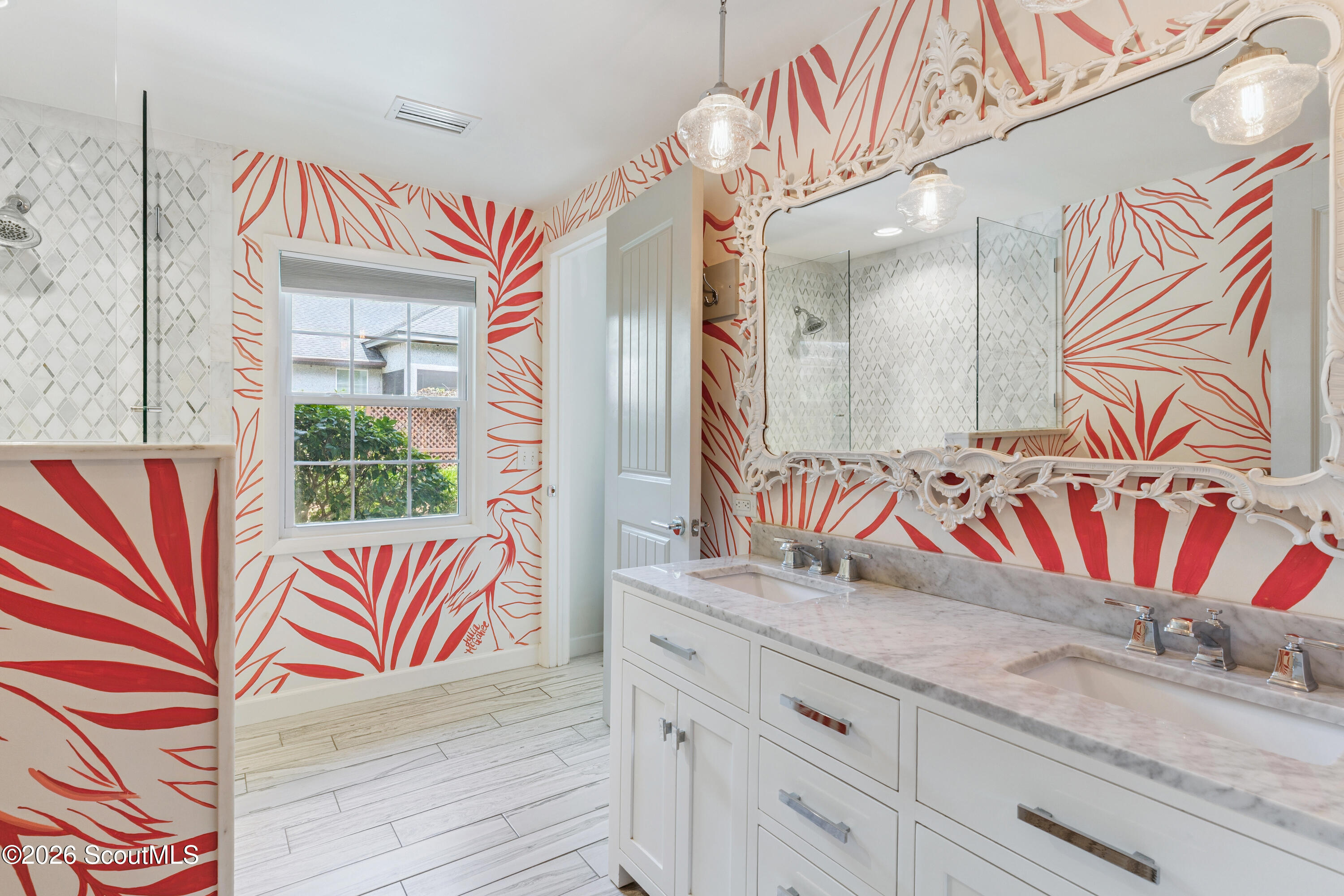 Bathroom with a double vanity, ornate mirror, red botanical wallpaper, and glass shower.