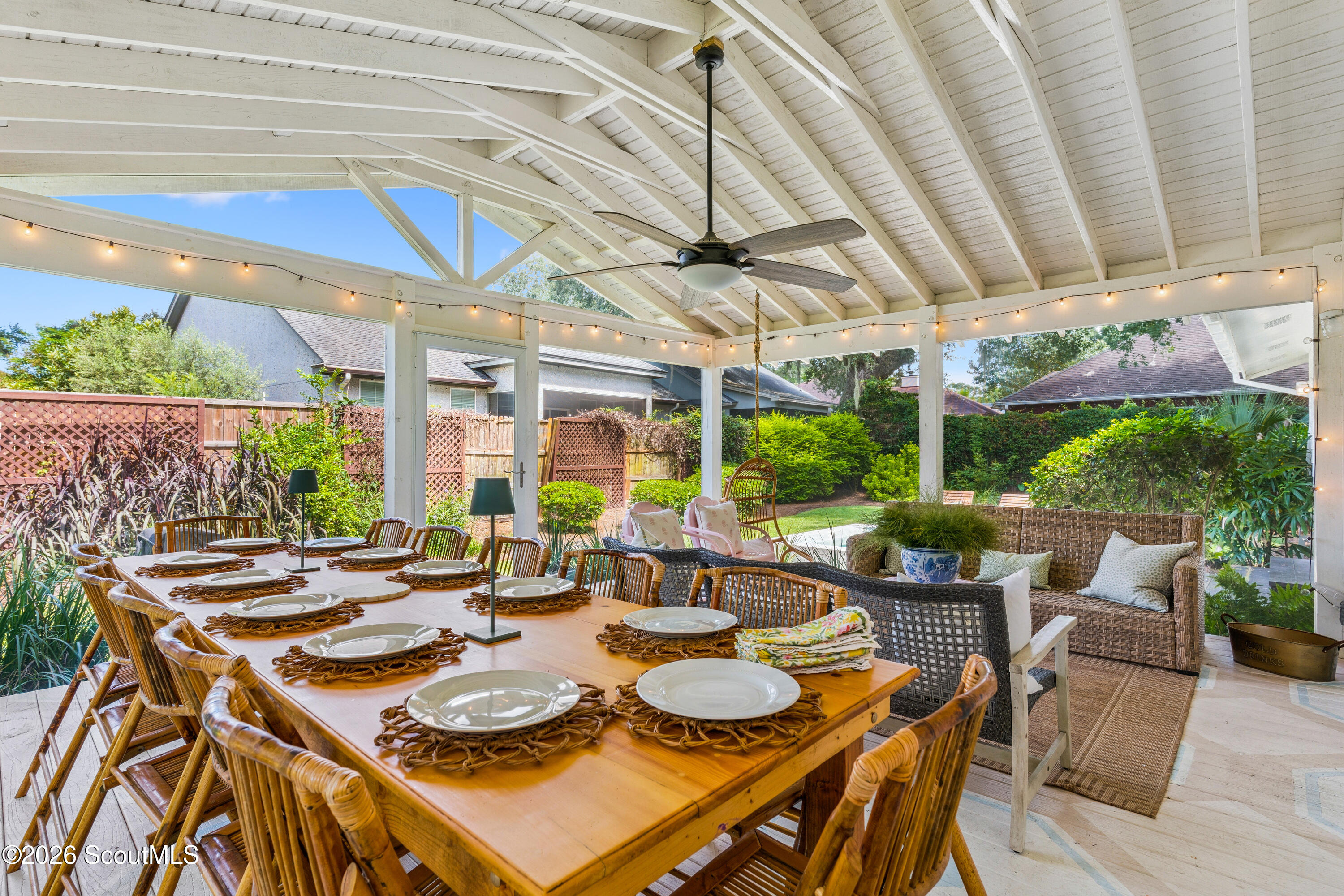 Covered porch with a set dining table, wicker lounge seating, ceiling fan, and string lights.
