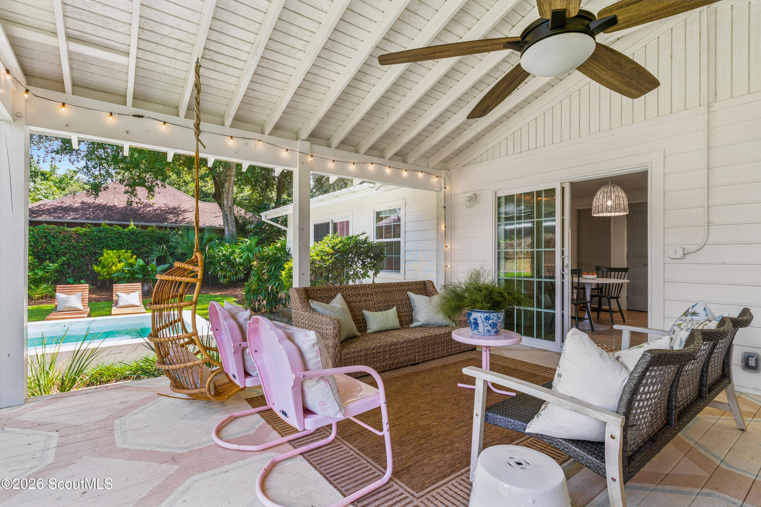 Covered patio with wicker seating, pink rocking chairs, and a view of the garden pool.