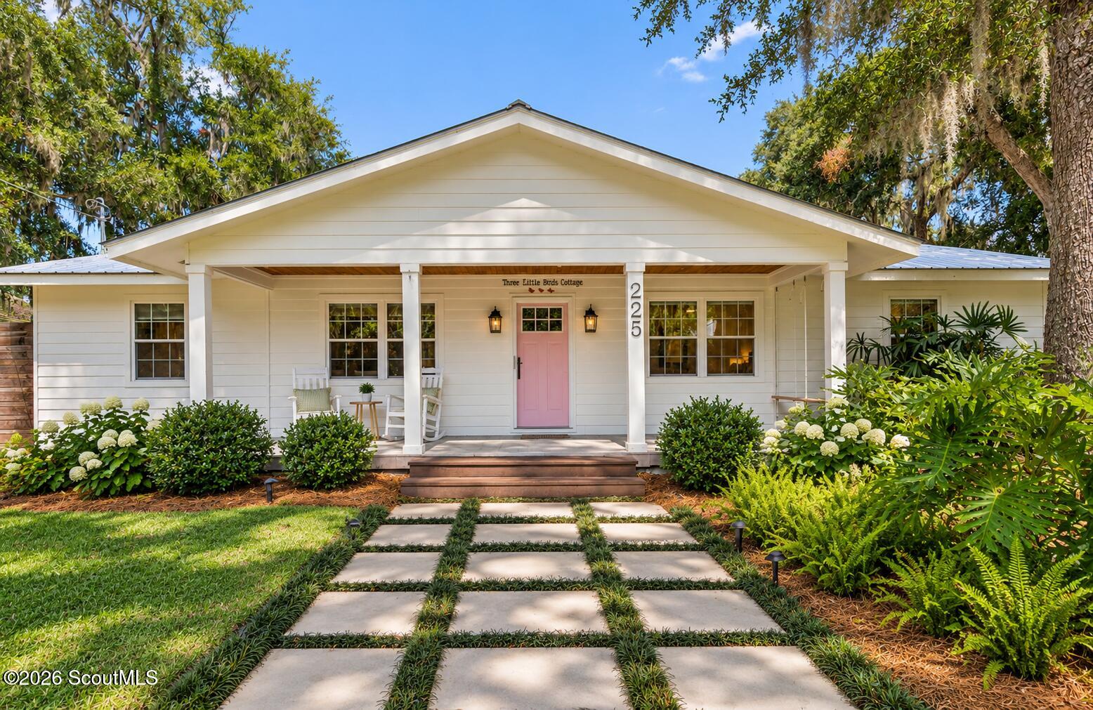White cottage with a covered porch, pink front door, and stepping-stone walkway.