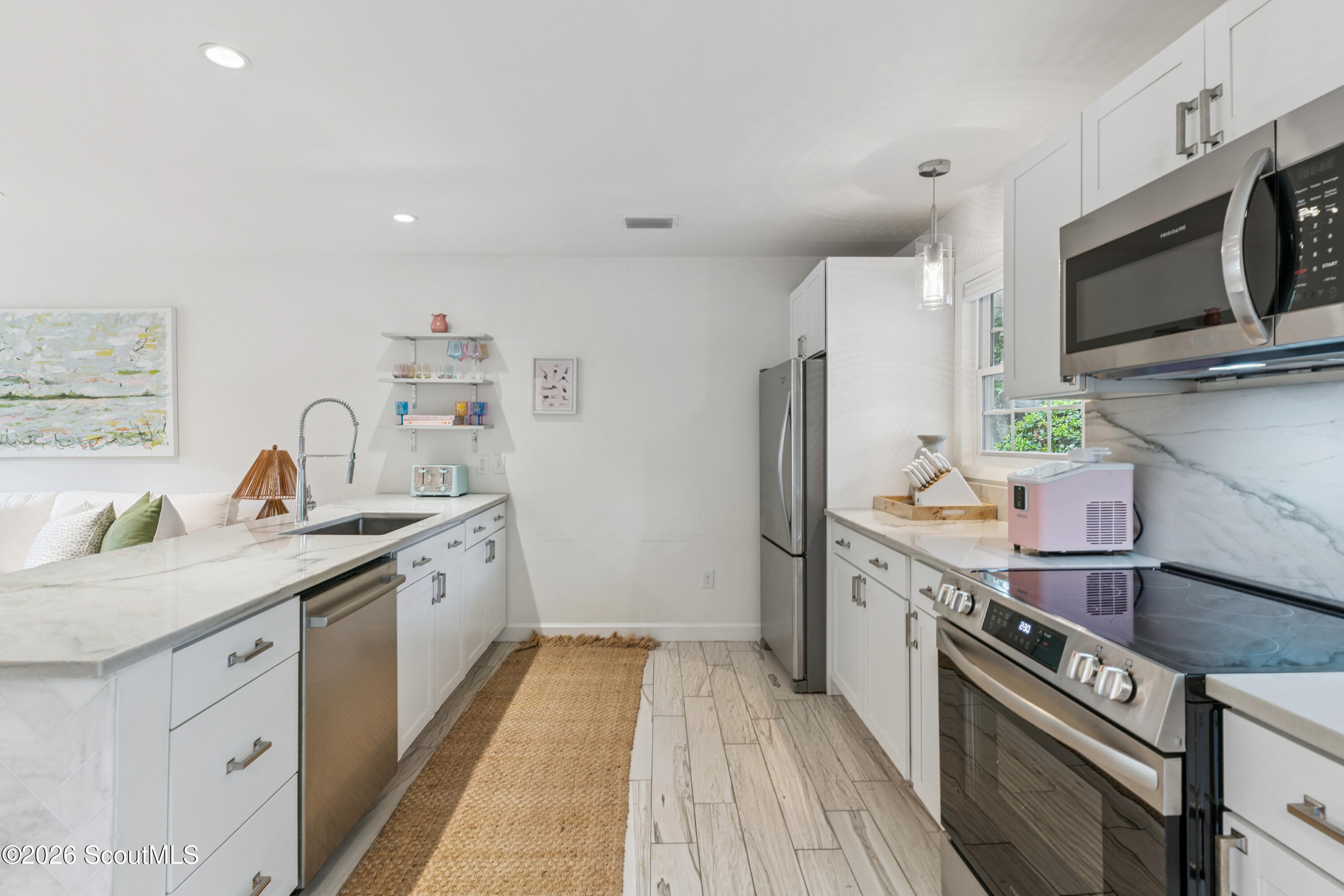 Bright white kitchen with a long marble-look island, stainless appliances, and a woven runner.