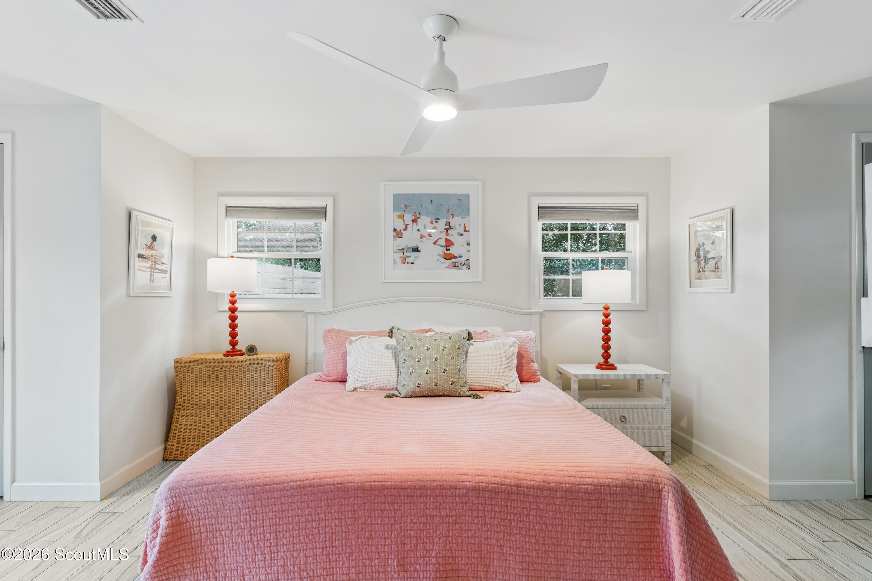 Furnished bedroom with a pink quilted bed, red accent lamps, and windows on either side of the headboard.