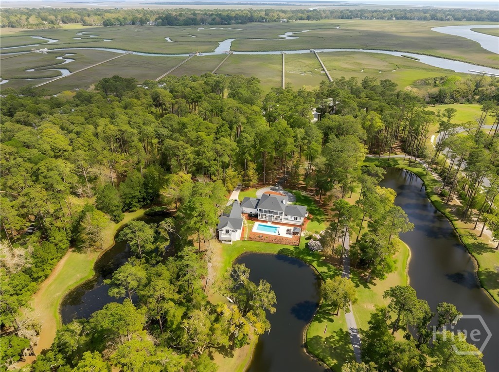 Aerial view of a wooded home with a swimming pool, ponds, and coastal marshland.