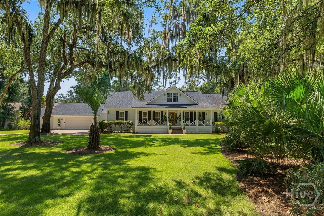 Home with a white-railed front porch and attached garage, framed by moss-draped oaks.