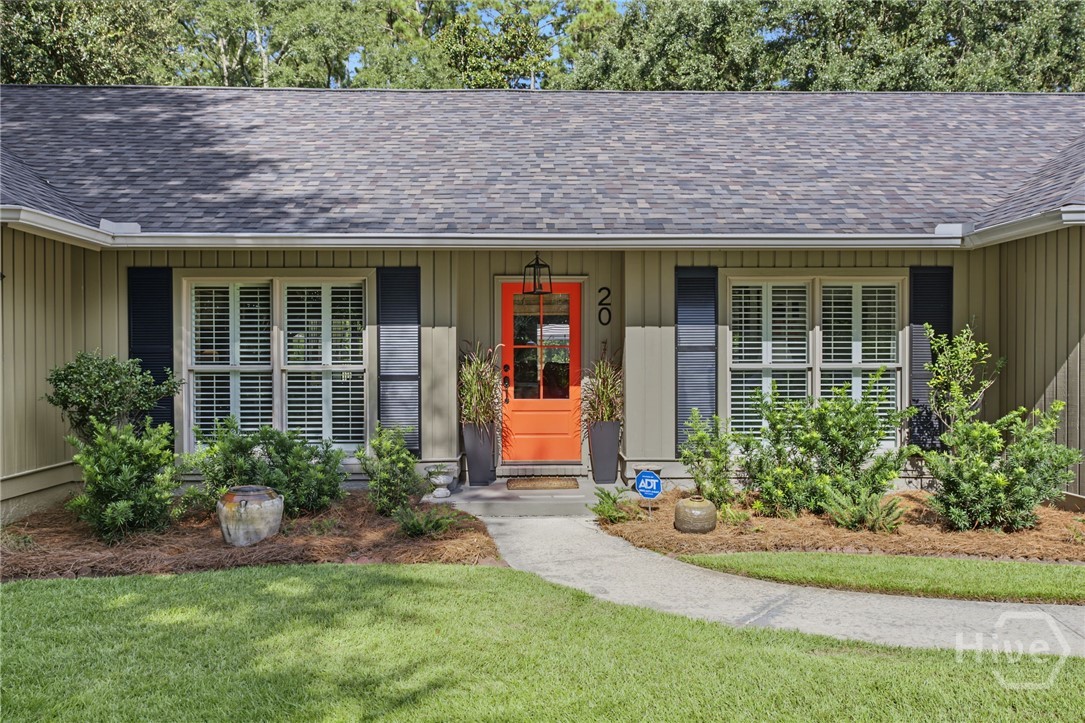 Single-story home with olive siding, dark shutters, and a bright orange front door.