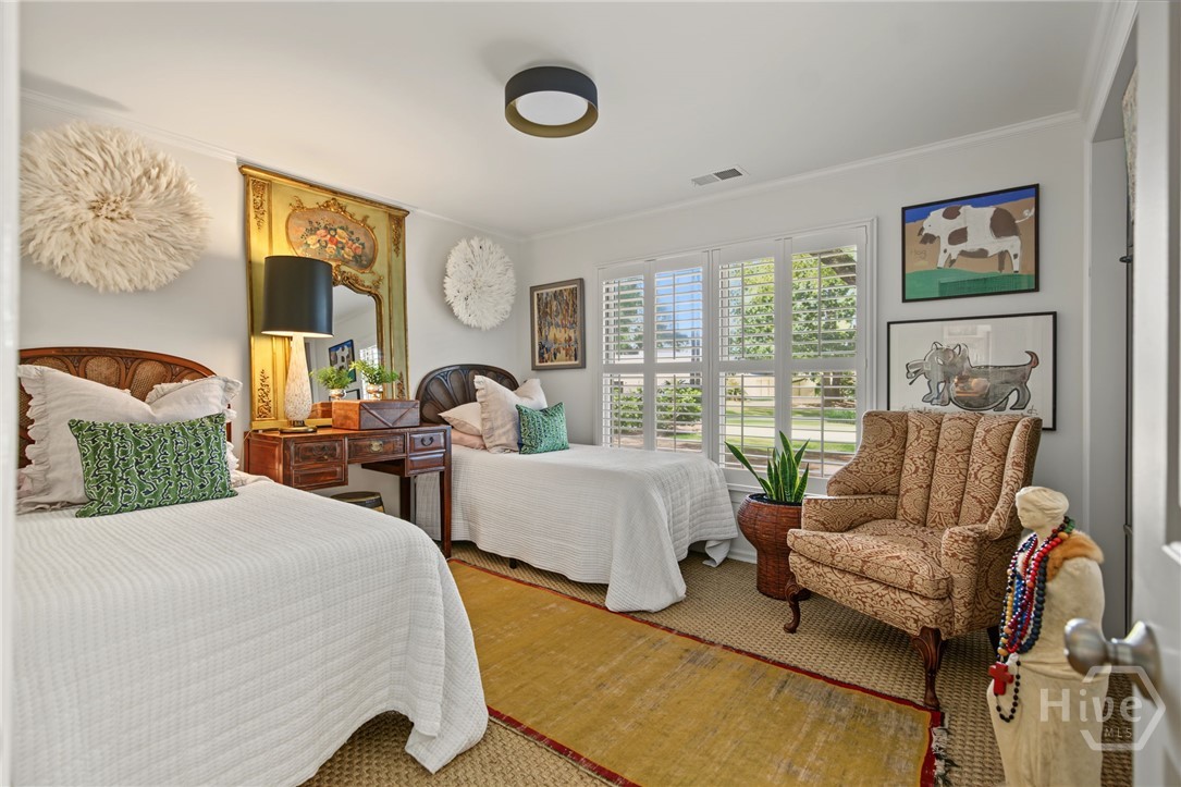 Bedroom with twin white beds, a wooden vanity, shuttered windows, and a patterned armchair.
