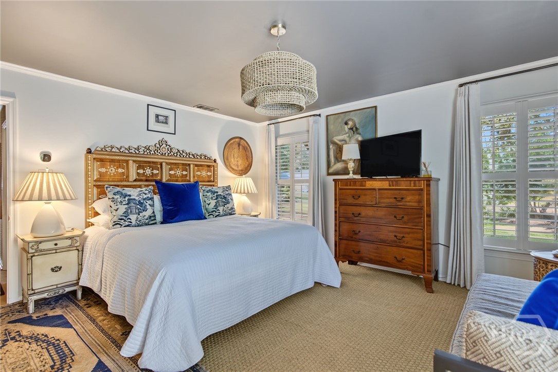 Bedroom with an ornate carved headboard, white bedding, wooden dresser, and plantation-shuttered windows.