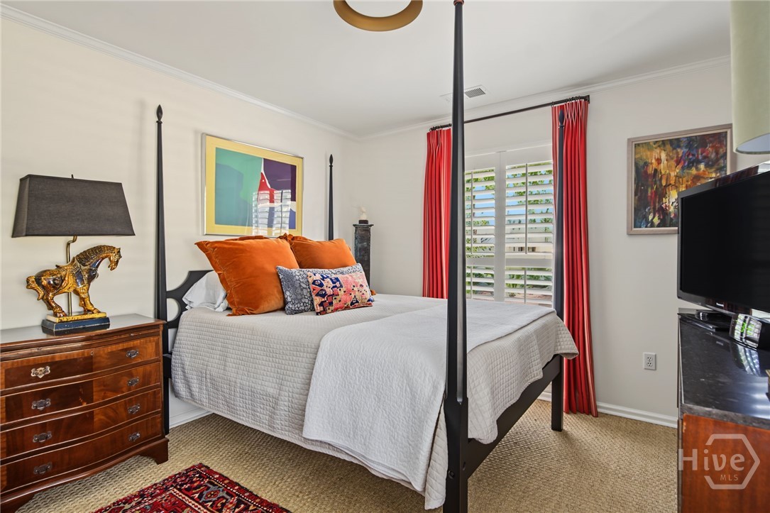 Bedroom with a black four-poster bed, orange pillows, and red curtains framing plantation shutters.