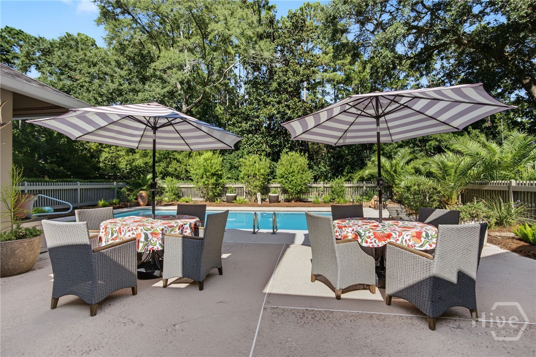 Backyard pool beside a patio with wicker dining chairs and two striped umbrellas.