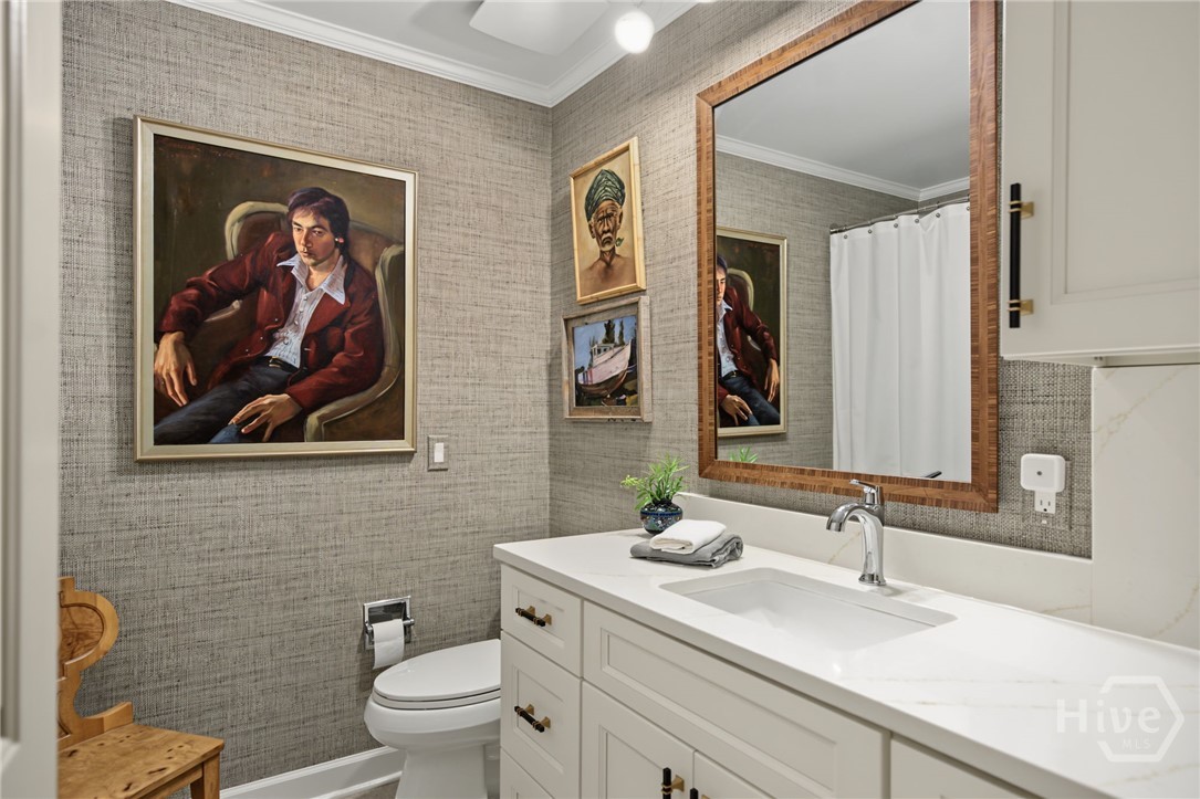 Bathroom with a white vanity, wood-framed mirror, textured gray walls, and framed artwork.