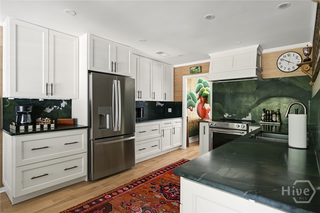 Kitchen with white cabinets, stainless appliances, dramatic green stone surfaces, and a colorful patterned rug.