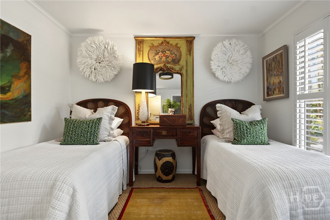 Bedroom with twin beds, an ornate gold-framed mirror, and white plantation shutters.