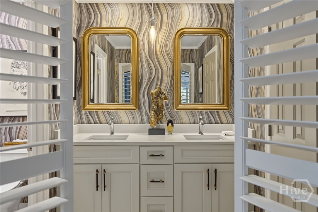 Bathroom vanity with two sinks, gold-framed mirrors, and wavy-patterned wallpaper.