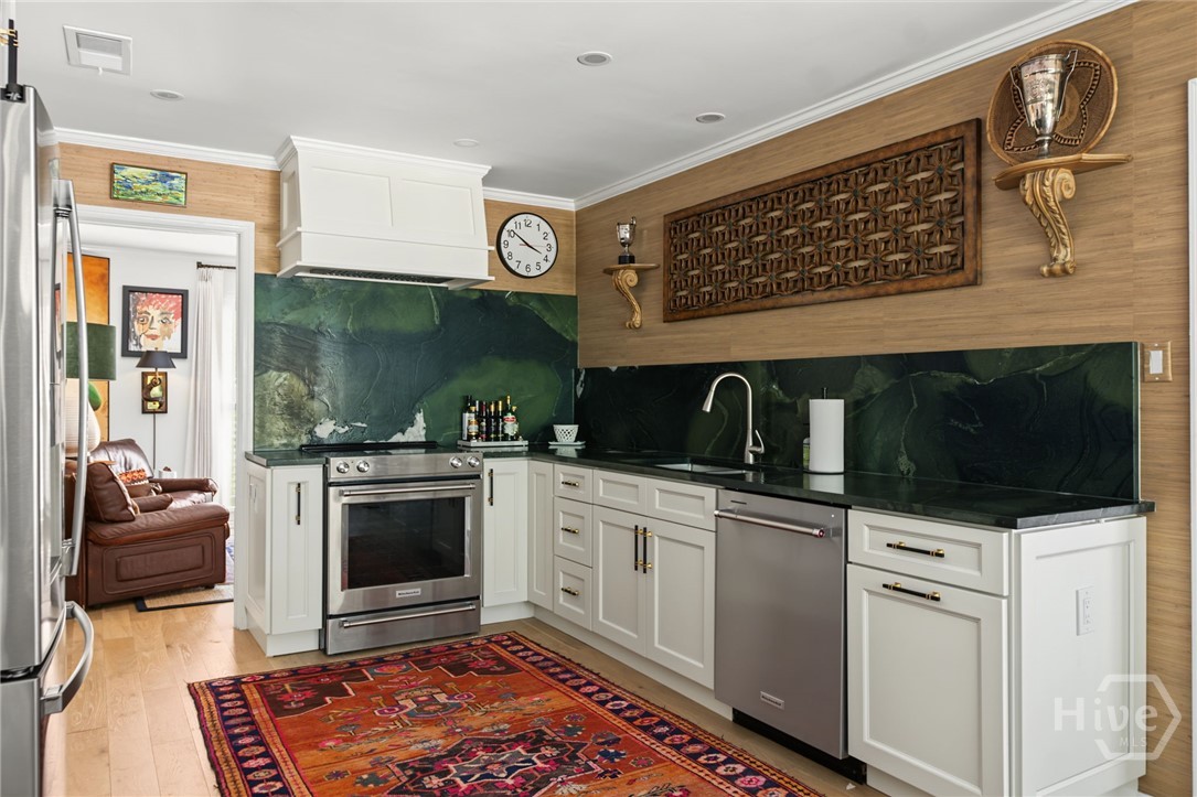 Kitchen with white cabinets, dramatic dark green stone surfaces, stainless steel appliances, and a colorful patterned rug.