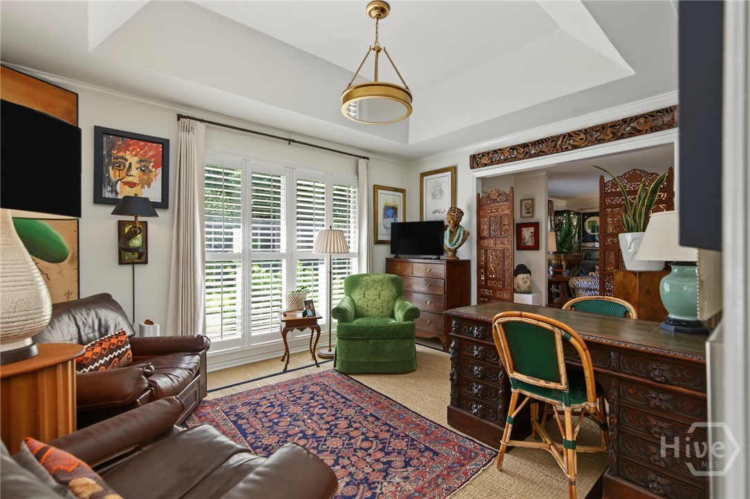Furnished study with carved wood desk, leather sofas, green armchair, and bright plantation-shuttered windows.