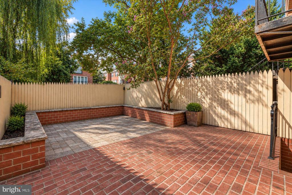 Brick courtyard patio with a raised tree planter, wooden privacy fence, and deck.